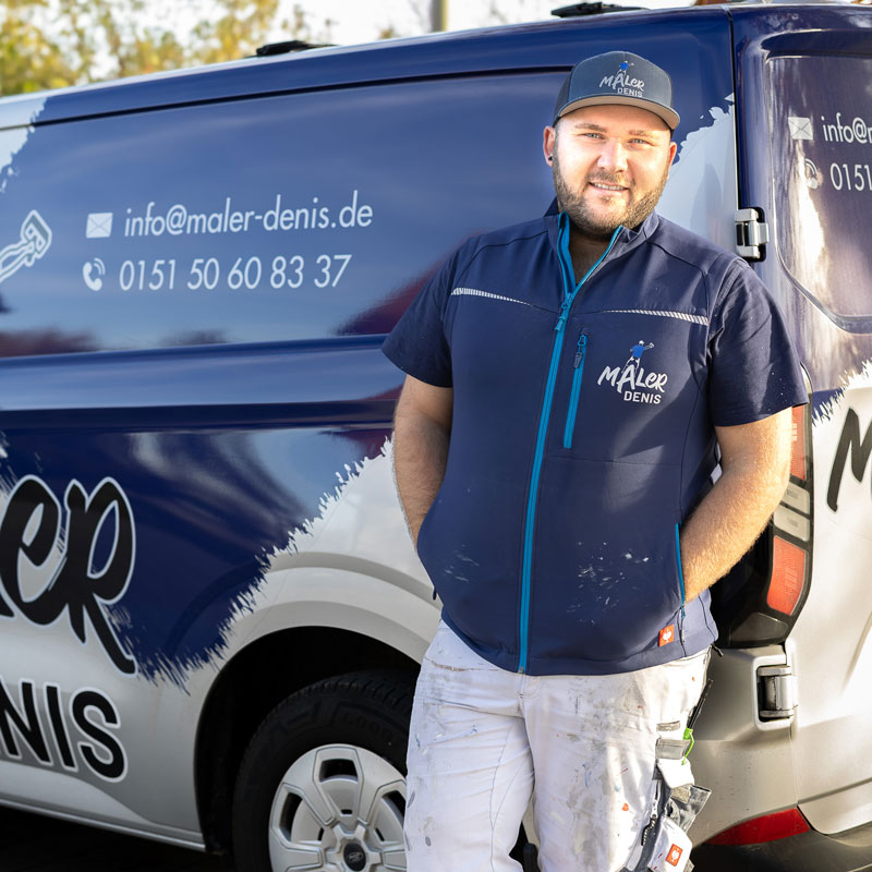 Ein Maler in Arbeitskleidung lehnt an seinem Firmenfahrzeug, das mit Logo, Kontaktdaten und Gestaltungselementen des Betriebs beschriftet ist. Der Maler trägt eine Kappe und eine Weste mit Firmenlogo. Die Szene vermittelt Professionalität, Kundenservice und mobile Einsatzbereitschaft eines modernen Malerbetriebs.